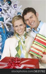 Couple holding presents by Christmas tree, portrait