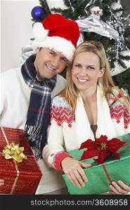 Couple holding presents in front of Christmas tree