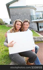 Couple holding whiteboard in front of their house
