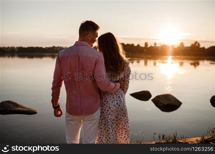 couple hugging at sunset. Beautiful young couple in love walking along the lake at sunset in the rays of bright light. selective focus. concept of family, comfort, safety.. couple hugging at sunset. Beautiful young couple in love walking along the lake at sunset in the rays of bright light. selective focus. concept of family, comfort, safety