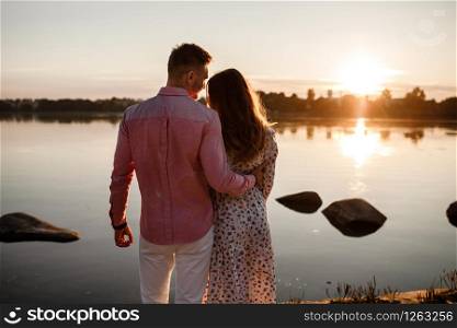 couple hugging at sunset. Beautiful young couple in love walking along the lake at sunset in the rays of bright light. selective focus. concept of family, comfort, safety.. couple hugging at sunset. Beautiful young couple in love walking along the lake at sunset in the rays of bright light. selective focus. concept of family, comfort, safety