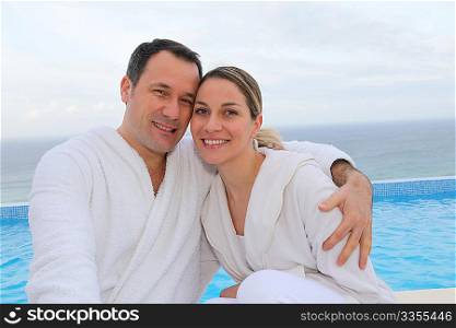Couple in bathrobe sitting by swimming-pool