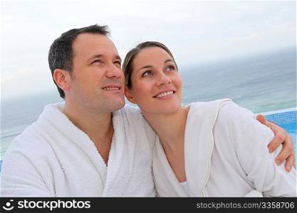 Couple in bathrobe sitting by swimming-pool