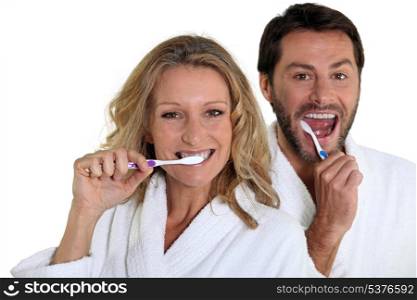 Couple in bathrobes cleaning teeth