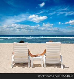 Couple in beach chairs holding hands near ocean