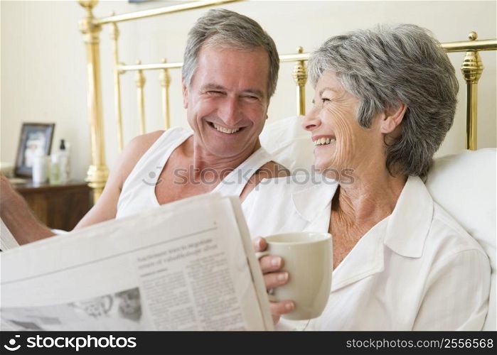Couple in bedroom with coffee and newspapers smiling