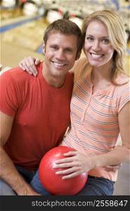 Couple in bowling alley holding ball and smiling
