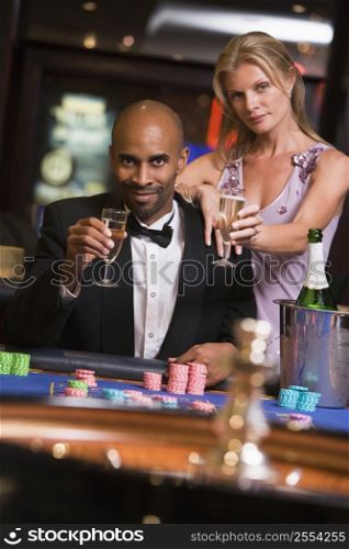 Couple in casino at roulette table holding champagne and smiling (selective focus)