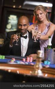Couple in casino at roulette table holding champagne and smiling (selective focus)