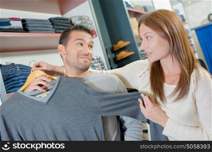Couple in clothes shop, lady holding jumper against man