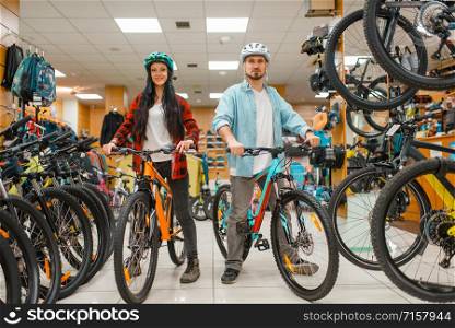Couple in cycling helmets choosing bicycles, shopping in sport shop. Summer season extreme lifestyle, active leisure store, customers buying cycles