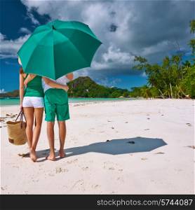 Couple in green with umbrella on a tropical beach at Seychelles