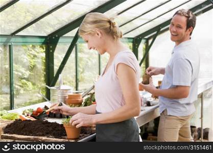 Couple in greenhouse putting soil in pots smiling
