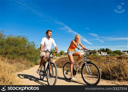 Couple in holidays cycling under a blue sky in the dunes