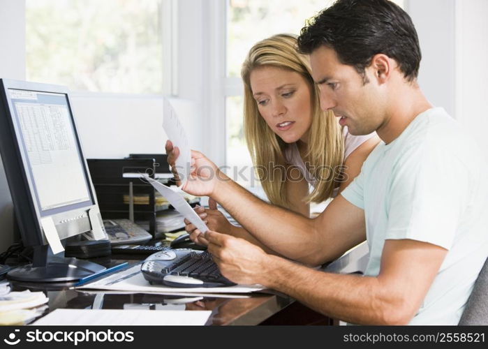 Couple in home office with computer and paperwork looking unhappy