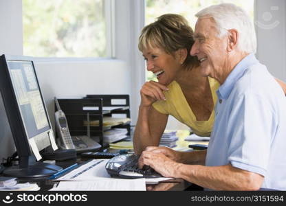 Couple in home office with computer and paperwork smiling