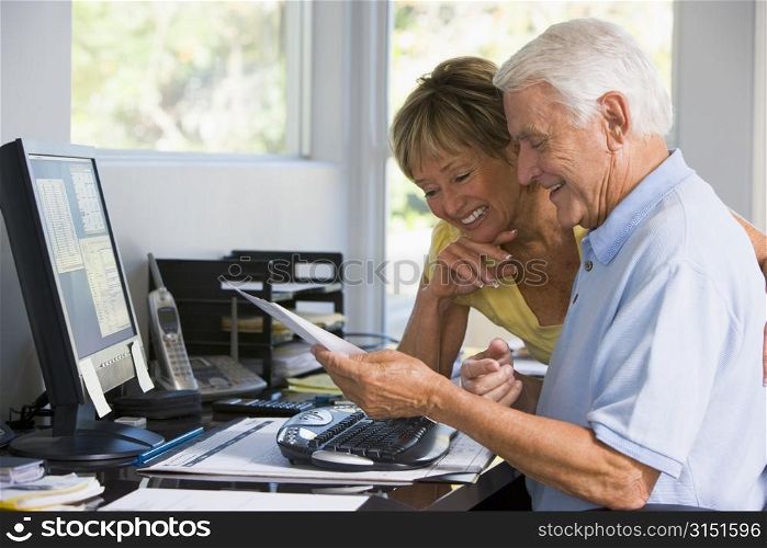Couple in home office with computer and paperwork smiling