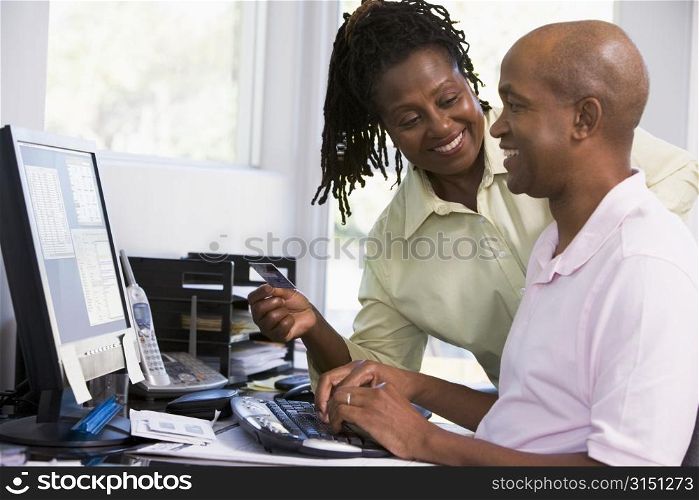Couple in home office with credit card using computer and smiling