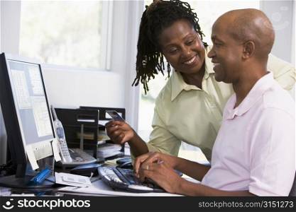 Couple in home office with credit card using computer and smiling