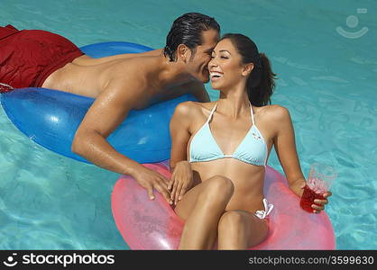 Couple in inflatable rings whispering in pool