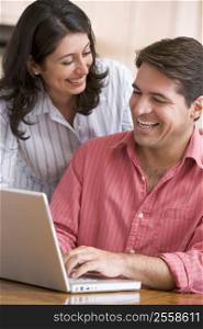 Couple in kitchen using laptop smiling