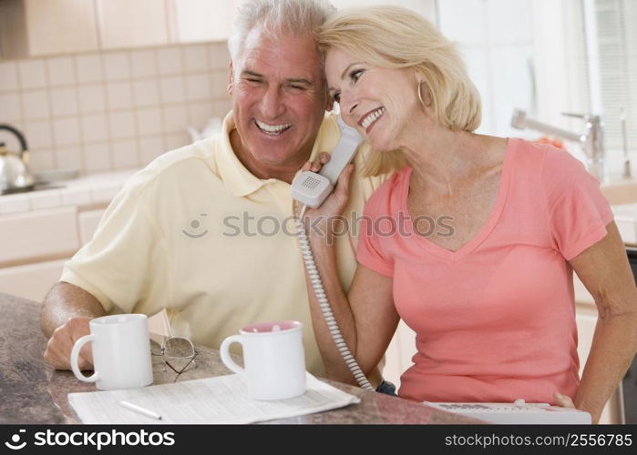 Couple in kitchen with coffee using telephone together and smiling