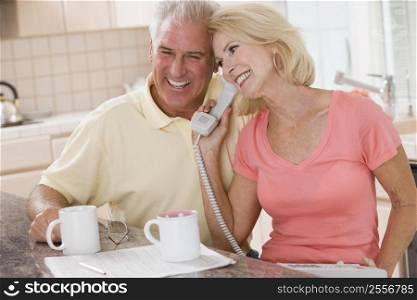 Couple in kitchen with coffee using telephone together and smiling