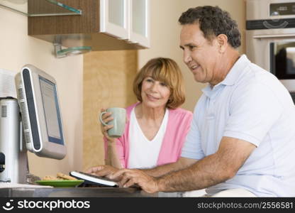 Couple in kitchen with computer and coffee smiling