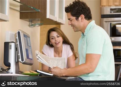 Couple in kitchen with computer and newspaper smiling