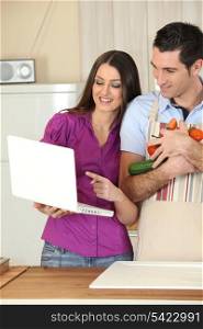 Couple in kitchen with computer and vegetables