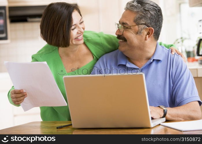 Couple in kitchen with laptop and paperwork smiling