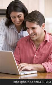 Couple in kitchen with paperwork using laptop smiling
