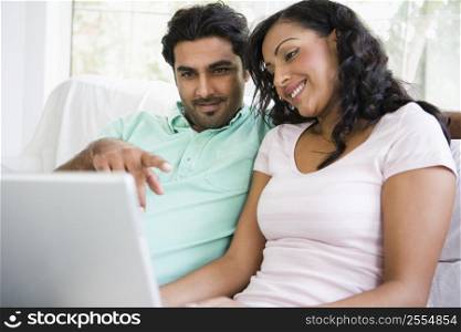 Couple in living room with laptop pointing and smiling (high key/selective focus)