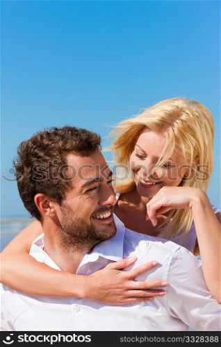 Couple in love - Caucasian man having his woman piggyback on his back under a blue sky on a beach