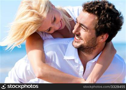 Couple in love - Caucasian man having his woman piggyback on his back under a blue sky on a beach
