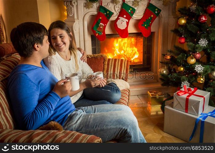 Couple in love drinking tea on sofa at burning fireplace decorated for Christmas