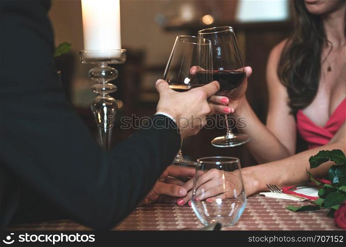 Couple in love holding hands and drinking wine during a romantic dinner in a restaurant (reduced tone)