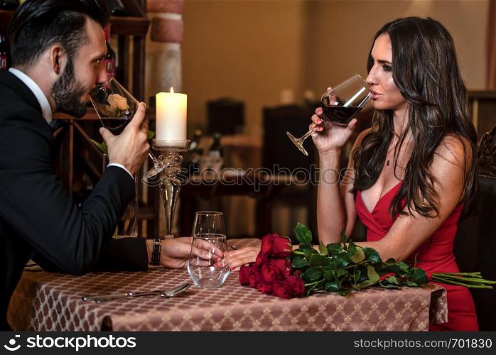 Couple in love holding hands and drinking wine during a romantic dinner at the restaurant.