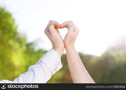 Couple in love making a heart shape with their hands outdoors. Man wearing elegant white shirt with cufflinks. . Couple in love making a heart shape with their hands outdoors.