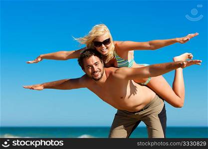 Couple in love - man carrying his wife on the back on a beach vacation, they are feeling visibly free and happy
