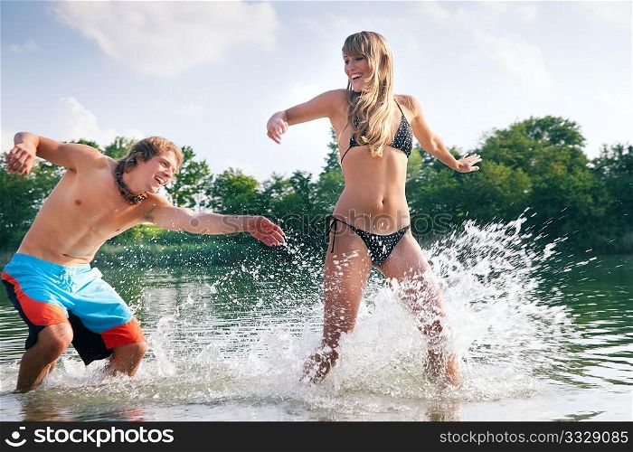 Couple in love on the beach of a lake - he is chasing her trying to splash some water on her in a playful way