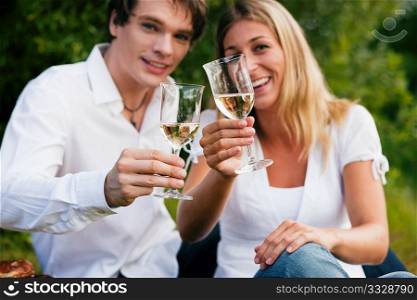 Couple in love sitting outdoors having a picnic clinking glasses and drinking white wine (focus on glasses!)