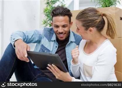 couple in new apartment sitting on floor and using tablet