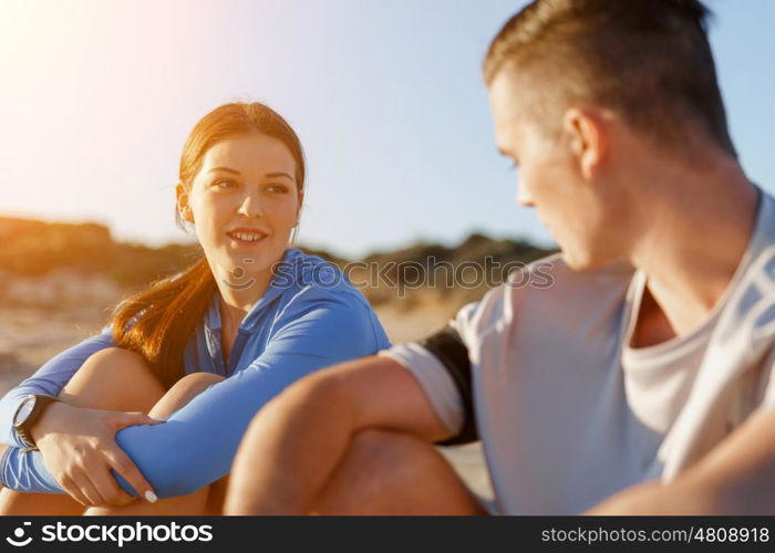 Couple in sport wear on beach. Young coulpe in sport wear sitting on beach