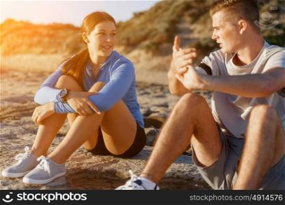 Couple in sport wear on beach. Young coulpe in sport wear sitting on beach