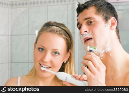 Couple in the bathroom, man shaving and woman brushing her teeth