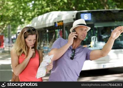 couple in the suburbs holding map and hailing a bus