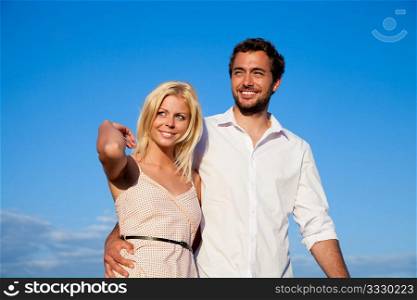 Couple in vacation having a walk under a perfect blue sky, they are embracing each other on shoulder