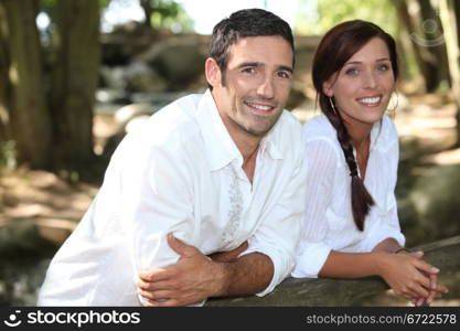 Couple in white leaning on a wooden fence