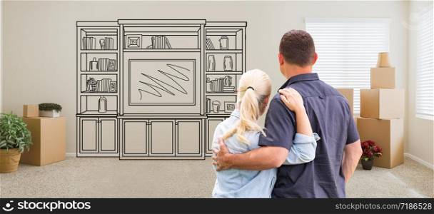 Couple Inside Empty Room with Moving Boxes Facing Entertainment Unit Drawing on Wall.